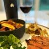 Bavette tranchée dans une assiette, accompagnée d'une salade de pommes de terre style grecque et d'un verre de vin rouge avec sa bouteille — un repas gourmet Pour Le Chef