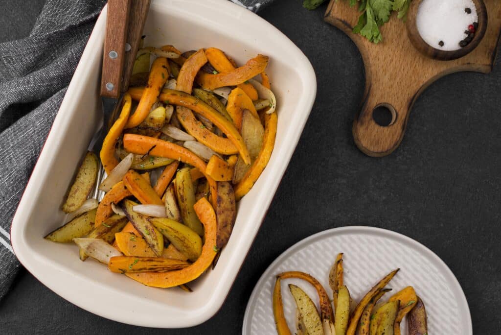 Roasted potato and carrot wedges seasoned with herbs in a white baking dish.