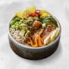 Close-up of a colorful poke-style bowl with rice, avocado chunks, edamame, pineapple, shredded carrot, cucumber, sesame seeds, and a savory sauce/condiment visible on top.