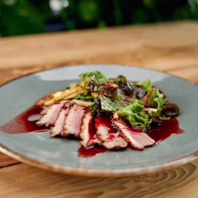 View from side of yummy snack on plate lying on table. Delicious ham with sauce and green cooked in luxurious restaurant for dinner. Concept of cuisine, appetizer and meal.