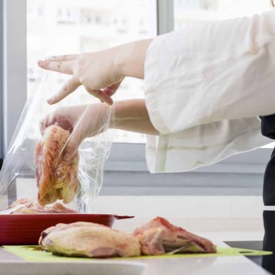 Person in a white coat packs baguette into a clear plastic bag on a kitchen counter near a window.